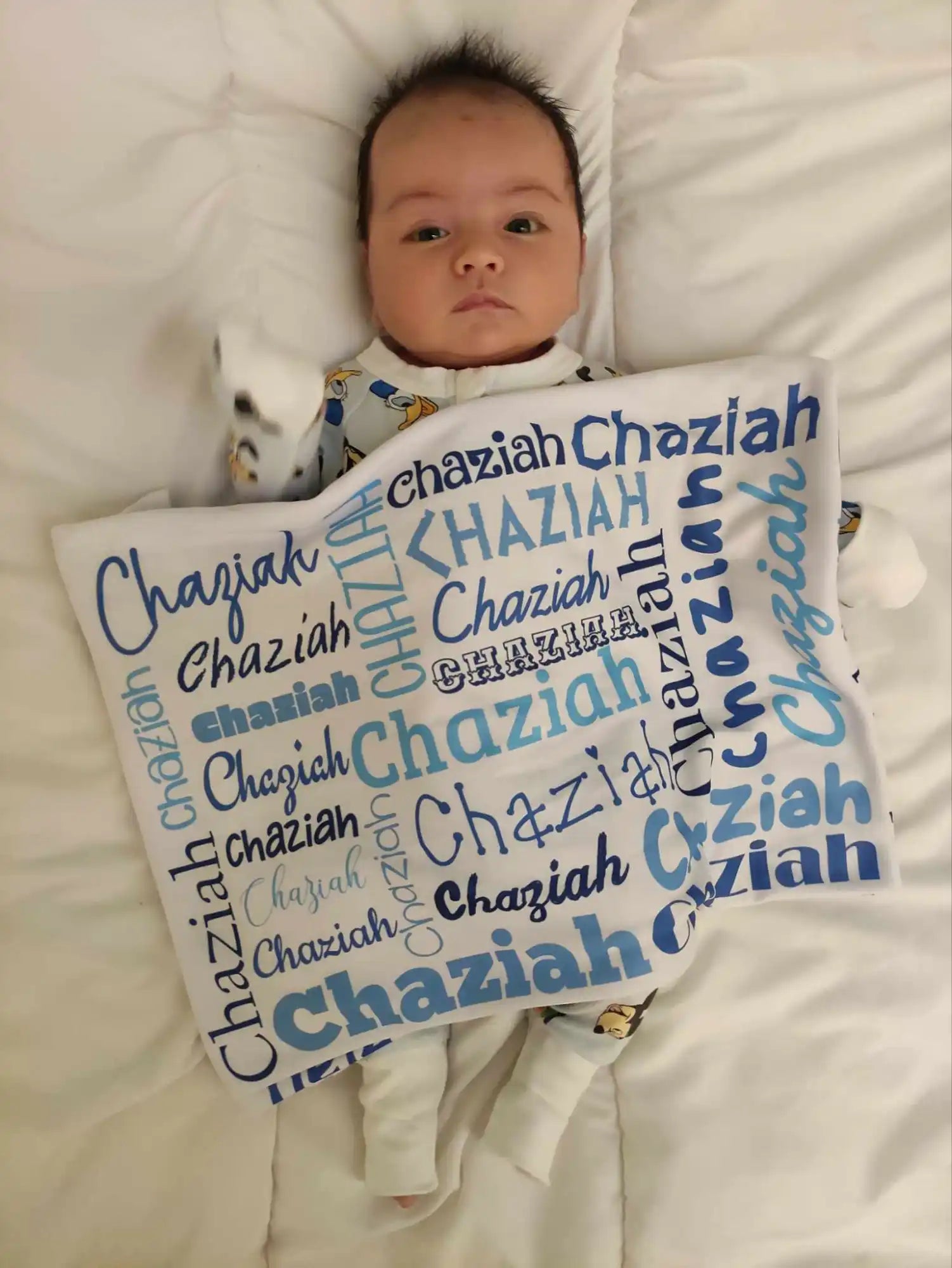 Baby lying on a blanket with repeated text of the name ’Chaziah’ in various fonts and colors.